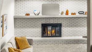 A living room with a white brick fireplace, a grey sofa with yellow cushions, and a small shelf above the fireplace with decorative items. - Modern 4BR Family Friendly Retreat W/ Hot tub (Arvada)