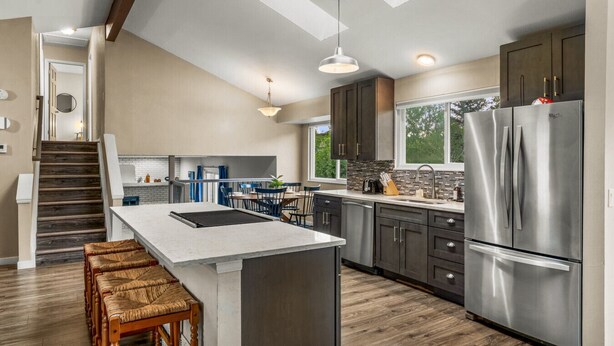 A modern kitchen with a central island, dark cabinets, stainless steel appliances, and a staircase leading to another level. - Modern 4BR Family Friendly Retreat W/ Hot tub (Arvada)