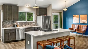 A modern kitchen with dark cabinets, stainless steel appliances, and a large island with bar stools. - Modern 4BR Family Friendly Retreat W/ Hot tub (Arvada)