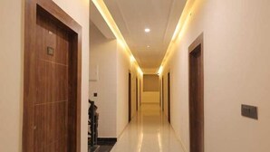 A long, narrow hallway with wooden doors on either side, a tiled floor, and recessed lighting along the ceiling. - PriyaKunj Dham Guest House (Mathura)