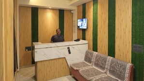 A reception area with a wooden reception desk, a sofa, a television, and a ceiling light. - PriyaKunj Dham Guest House (Mathura)