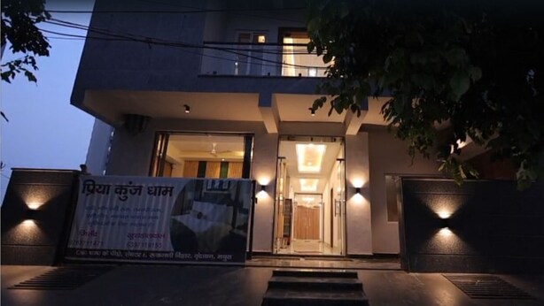 A modern building with a well-lit entrance, a visible signboard, and a staircase leading to the door. - PriyaKunj Dham Guest House (Mathura)