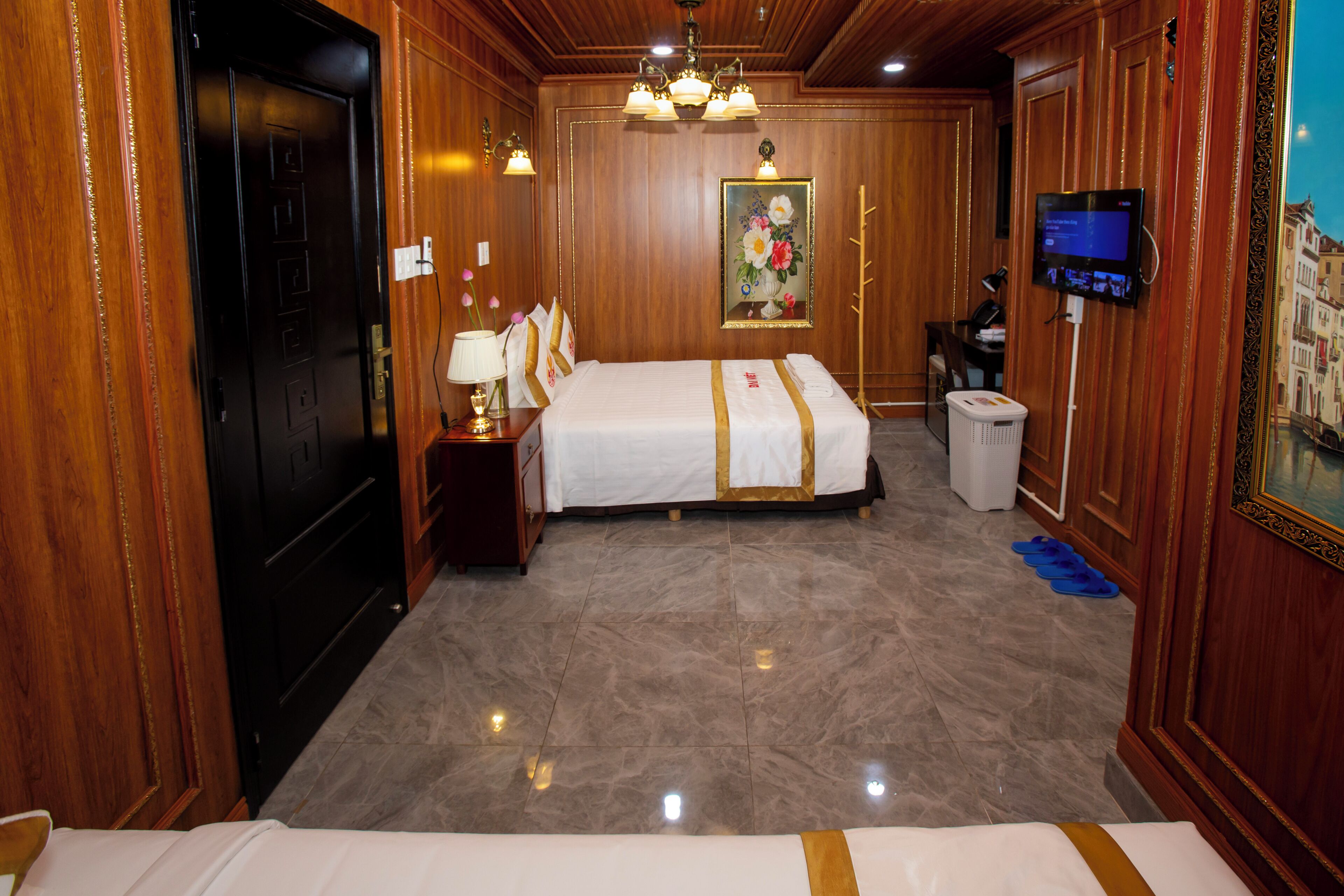 A hotel room with a bed, a desk, a television, and a painting on the wall.