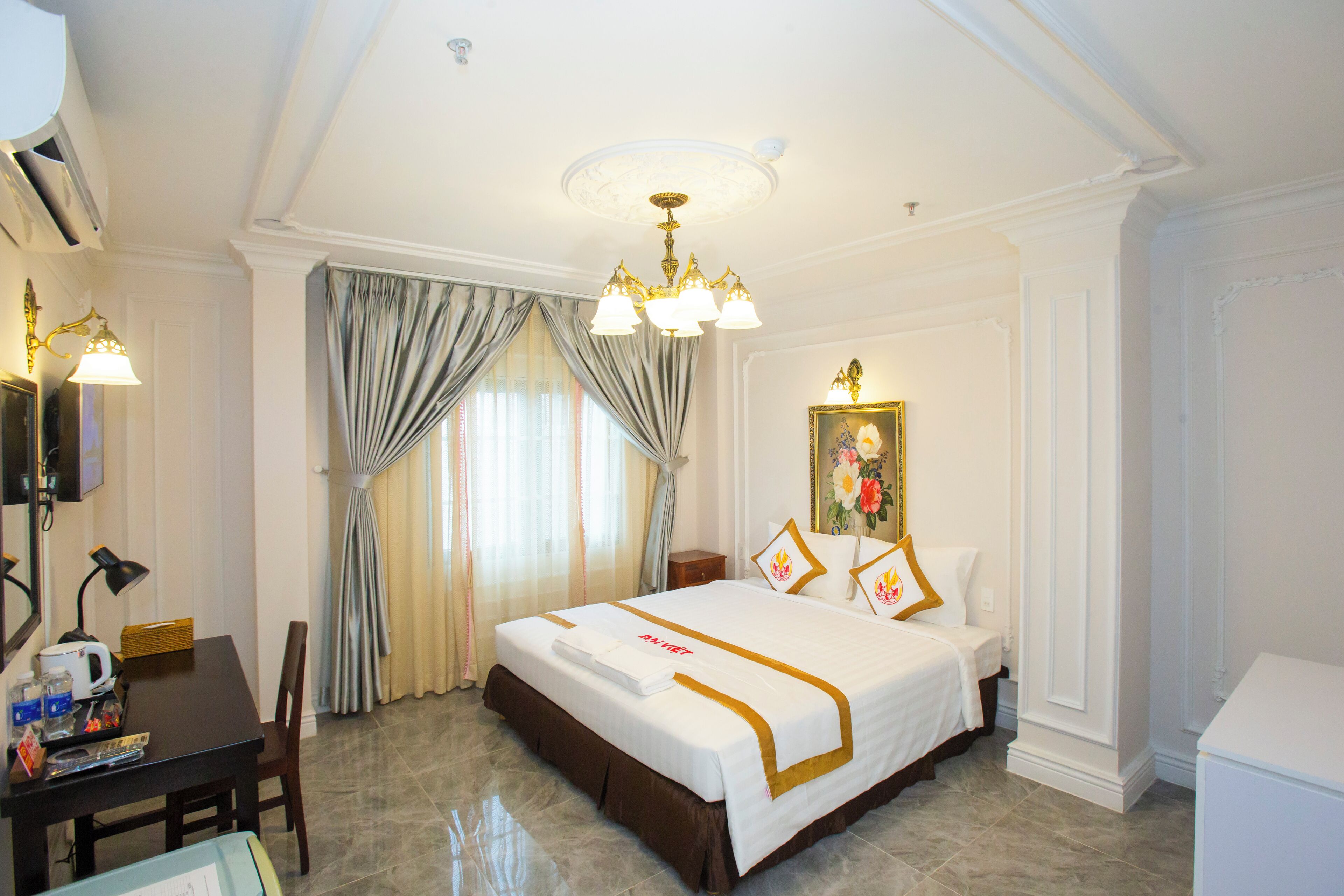 A hotel room with a large bed, a desk with a lamp, and a picture frame on the wall.