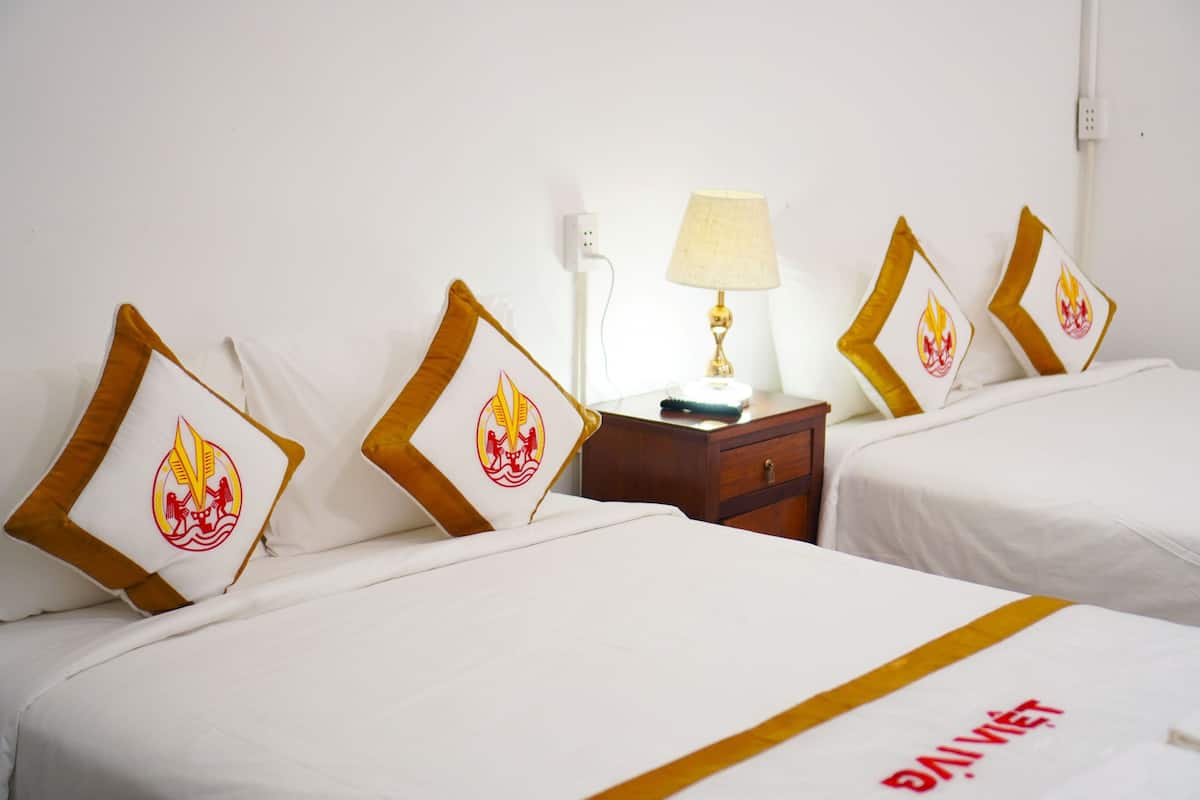 A hotel room with two beds, each with a white bedspread and a pillow featuring a flame design. There is a nightstand with a lamp between the beds.