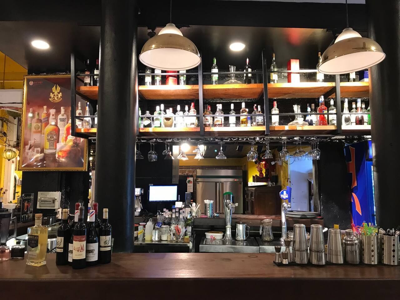 Zona de bar con múltiples estantes de botellas de licor, una barra con diversos utensilios y lámparas colgantes.