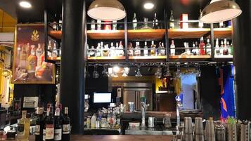 Zona de bar con múltiples estantes de botellas de licor, una barra con diversos utensilios y lámparas colgantes.