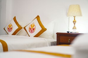 A hotel room with a neatly made bed, two pillows with a flame design, a bedside table with a lamp, and a wall-mounted power outlet. - The Rice Hotel & Tour - 180 Bui Vien (Ho Chi Minh City)