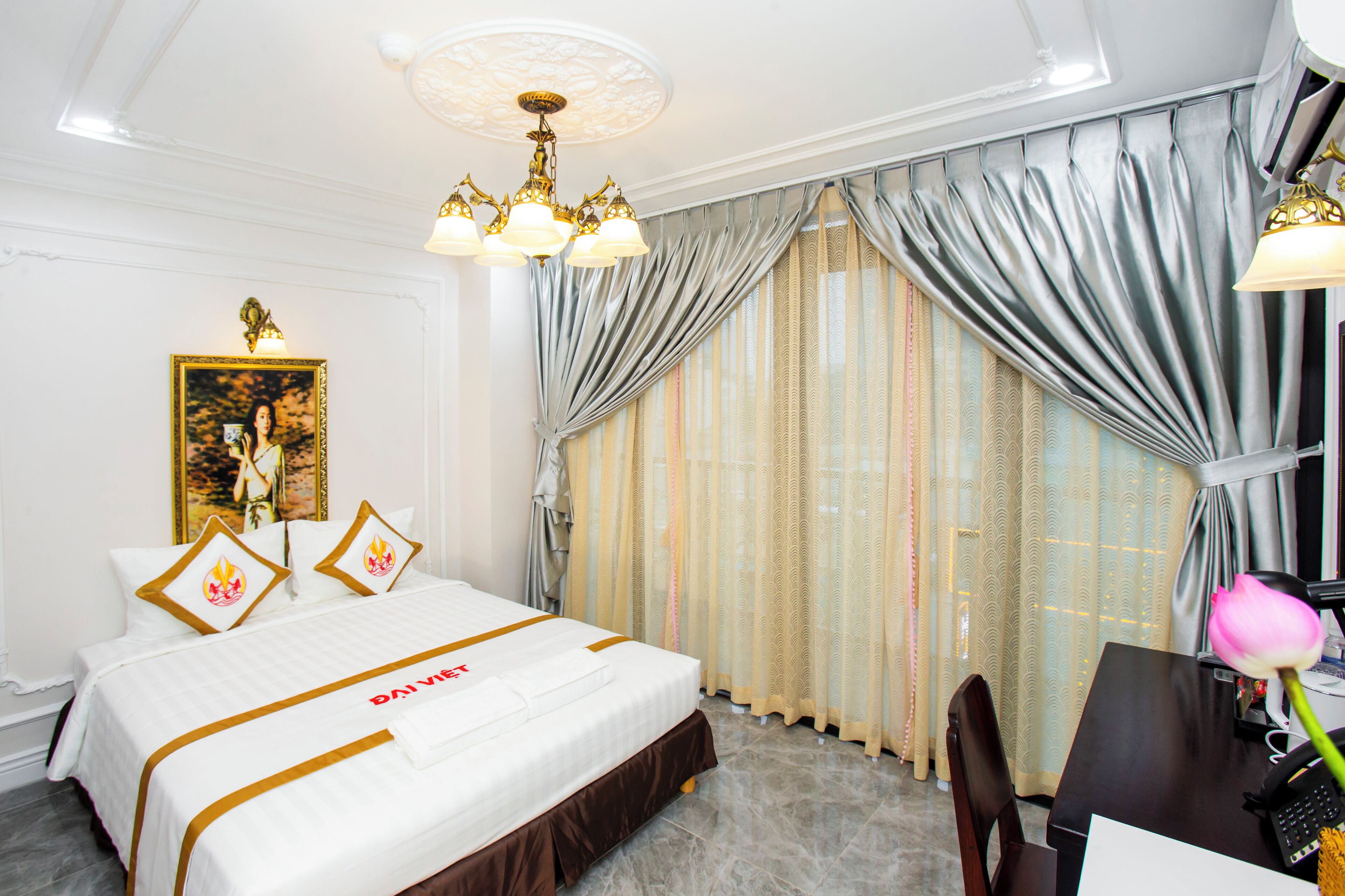 Ein Hotelzimmer mit einem ordentlich bezogenen Bett, einem Schreibtisch mit Computer und einem großen Fenster mit Vorhängen.