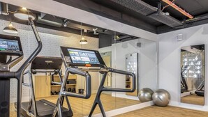 A gym with exercise equipment, a digital screen, and a mirrored wall. - Dünenloft, House Düne Whg. 12 - Dünenlofts (Sylt)