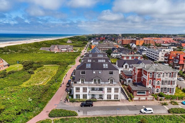 A coastal town with a prominent building featuring a steep roof and a balcony, surrounded by residential houses and a beach in the background.