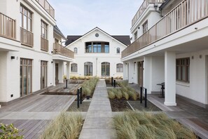 A courtyard with a central pathway, surrounded by buildings with balconies and large windows.