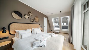 Et moderne soveværelse med en stor seng, et natbord, en lampe og udsigt udendørs gennem store vinduer.