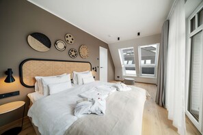 A modern bedroom with a large bed, a bedside table, a lamp, and a view of the outside through large windows.