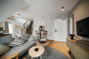 A modern living room with a grey sofa, wooden coffee table, and a TV mounted on the wall. - Dünenloft, House Düne Whg. 12 - Dünenlofts (Sylt)