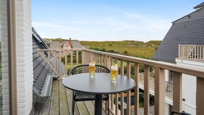 En balkon med et rundt bord og to ølglas, med udsigt over et græsareal og en bygning i det fjerne.