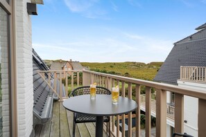 A balcony with a round table and two glasses of beer, overlooking a grassy landscape and a distant building.