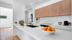 A modern kitchen with white countertops, a wooden cabinet, a sink, and a bowl of oranges.