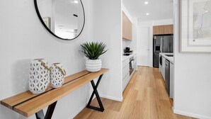 A modern kitchen with stainless steel appliances, a wooden bench with decorative vases, and a potted plant.