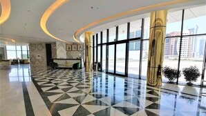 A spacious lobby with a geometric patterned floor, large windows offering views of the city, and a reception desk.