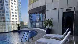 A rooftop pool area with a glass balustrade, two lounge chairs, and potted plants.