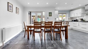 Una cocina moderna con armarios blancos, un comedor con mesa y sillas de madera, y vistas al exterior a través de amplios ventanales.