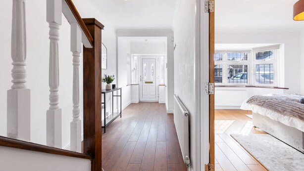 Un pasillo con una escalera de madera, una puerta blanca y una cama con una manta gris.