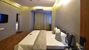 A hotel room with a bed, a flat-screen TV mounted on the wall, a ceiling fan, and an air conditioning unit. - Hotel Evergreen  (Mumbai)