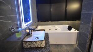 A modern bathroom with a marble sink, a bathtub, and dark tiled walls. - Hotel Evergreen  (Mumbai)