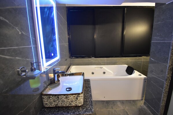 Un baño moderno con lavamanos de mármol, bañera y paredes de azulejos oscuros.