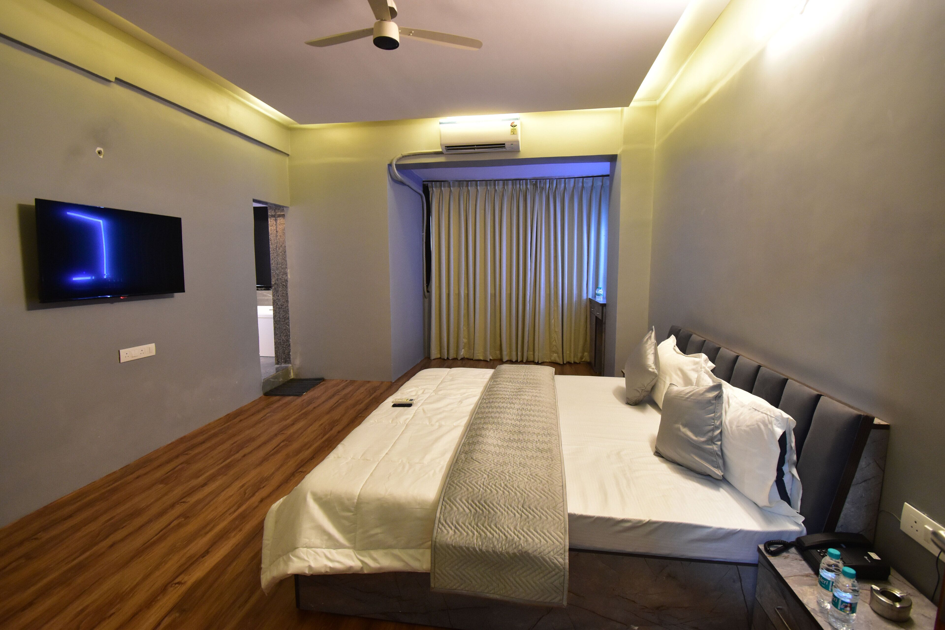 Habitación de hotel con cama, televisión de pantalla plana, aire acondicionado y ventilador de techo.