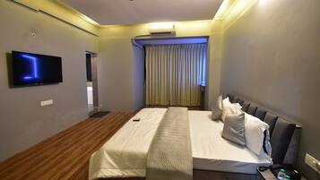 Habitación de hotel con cama, televisión de pantalla plana, aire acondicionado y ventilador de techo.