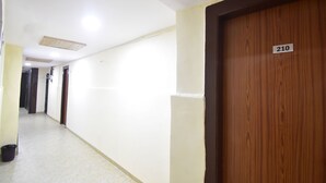 A hallway with a wooden door marked 210, white walls, and a tiled floor. - Hotel Evergreen  (Mumbai)
