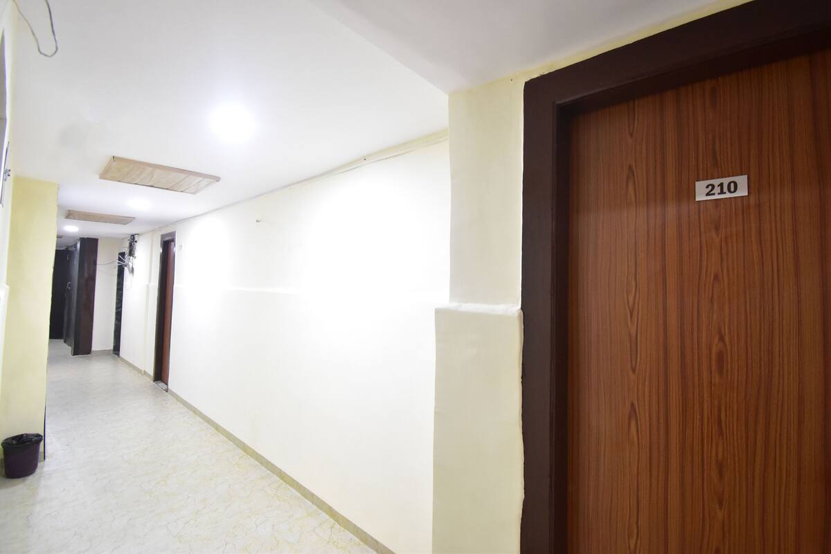 A hallway with a wooden door marked 210, white walls, and a tiled floor.