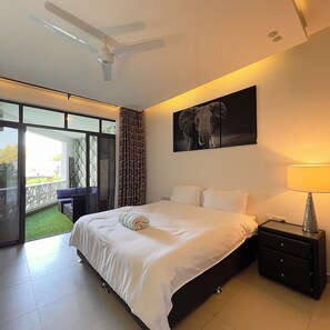 A bedroom with a bed, a nightstand, a lamp, a ceiling fan, a large window, and a sliding door leading to a balcony.