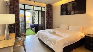 Una camera d'albergo con un letto, una scrivania, una sedia, un comodino, una ventola a soffitto e un'ampia finestra.