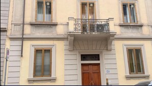 A building with a central entrance, multiple windows, and a balcony with a metal railing.