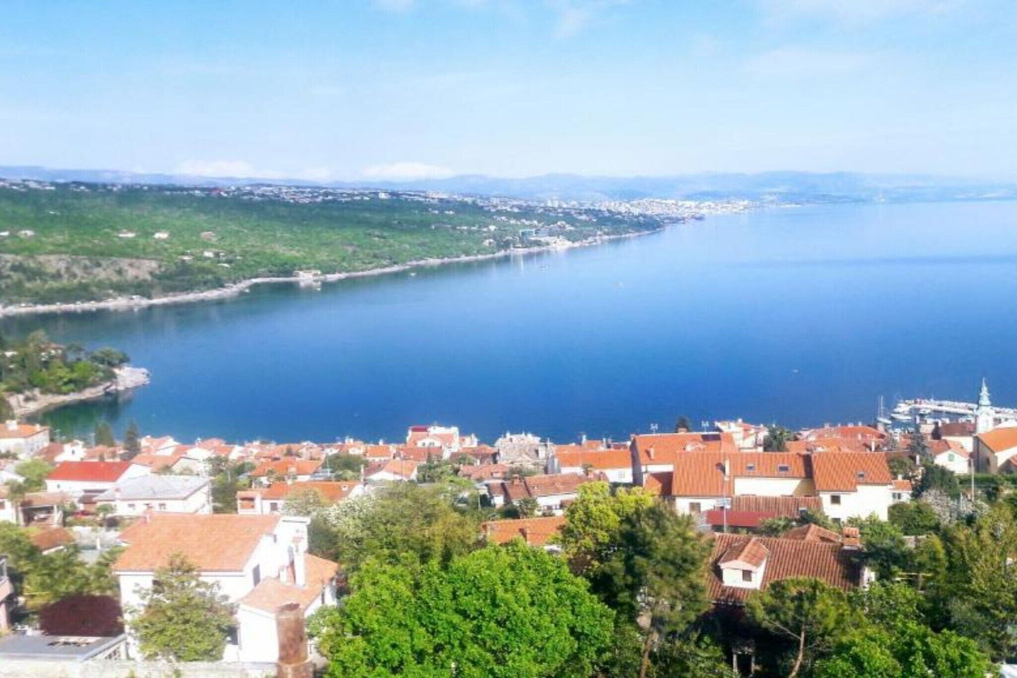Une ville côtière avec des bâtiments le long du front de mer, une vue dégagée sur la mer et un paysage vallonné en arrière-plan.