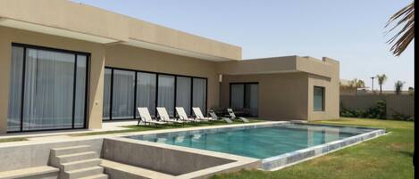A modern poolside area with a swimming pool, lounge chairs, and a staircase leading to a building with large windows.