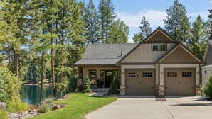 Une maison à deux étages avec un garage, une allée et un lac en arrière-plan.