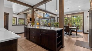 Une cuisine spacieuse dotée d’un grand îlot central, de poutres en bois et offrant une vue sur l’extérieur.
