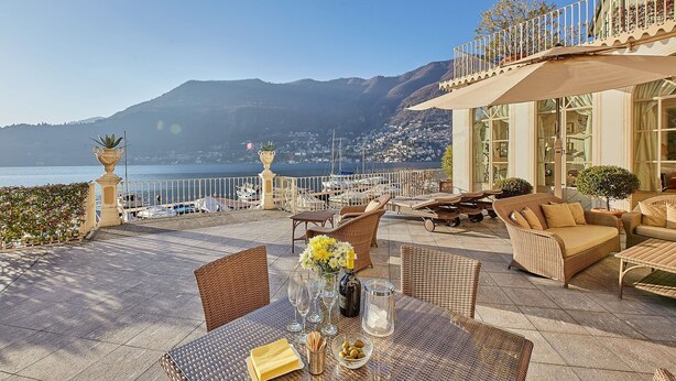 An outdoor terrace with wicker furniture, a table set for dining, and a view of the sea and mountains. - Villa Silva wiht pool - My Rental Homes (Torno)