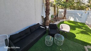 A patio area with a black Galaxy S23 Ultra sofa, a white chair, and two metal side tables. - Lovely studio with AC in Haifa (Haifa)