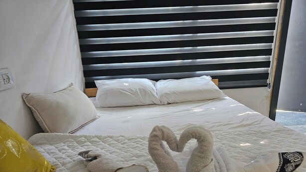 A neatly made bed with white bedding, a heart-shaped towel arrangement, and a 'Love' sign on the pillow. - Lovely studio with AC in Haifa (Haifa)