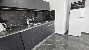 A modern kitchen with dark cabinetry, a marble backsplash, and a white refrigerator. - Lovely studio with AC in Haifa (Haifa)