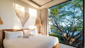 A bedroom with a large bed, a macrame wall hanging, a hanging lamp, and a view of trees through a large window. - Maitri ❤️ 2 BR | 3 BA | Private Pool | Villa | Fast Wifi (Tamarindo)