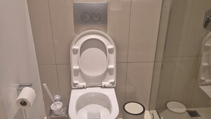 Un baño moderno con inodoro, bidé y un pequeño cubo de basura.