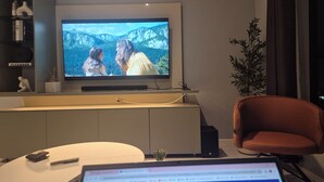 Una sala moderna con un televisor de pantalla plana montado en la pared, una computadora portátil sobre una mesa de centro y un sillón rojo.