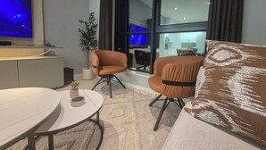Una sala de estar moderna con un sofá, una mesa redonda, un televisor y un ventanal grande.