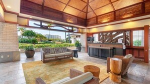 A spacious indoor area with a high ceiling, a seating area with sofas and chairs, a kitchen area with a counter, and a view of greenery outside. - Stunning Ocean View Luxury Suite - Ko Olina Beach Villas O421 End Unit (Kapolei)